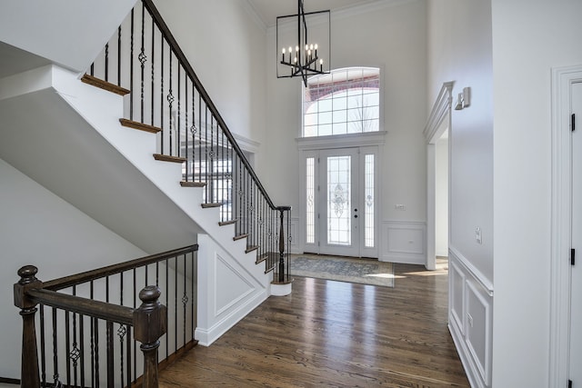 entryway featuring dark wood-style floors, a wainscoted wall, ornamental molding, a towering ceiling, and a decorative wall