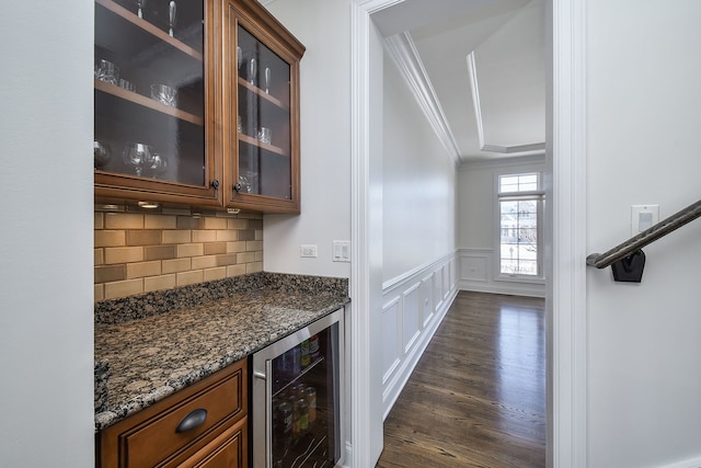 bar with beverage cooler, a wainscoted wall, ornamental molding, dark wood-style floors, and a bar