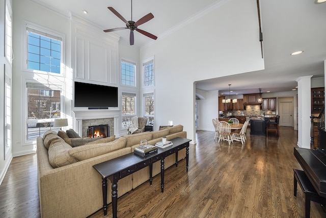 living area featuring dark wood finished floors, crown molding, a fireplace, and a ceiling fan