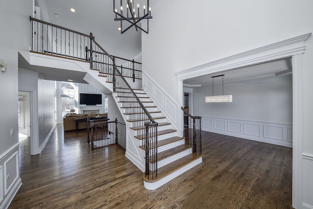 stairway with wood finished floors, a high ceiling, ornamental molding, and a decorative wall