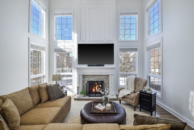 living room with dark wood finished floors, a stone fireplace, plenty of natural light, and baseboards