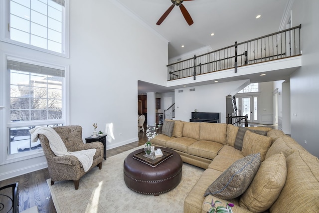 living area with wood finished floors, french doors, a high ceiling, crown molding, and baseboards