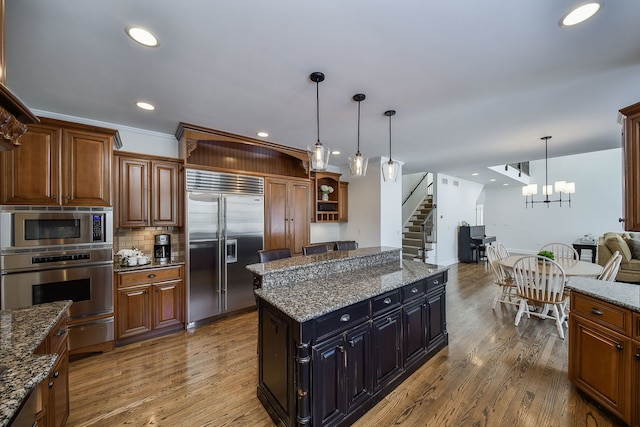 kitchen featuring decorative backsplash, wood finished floors, built in appliances, and pendant lighting