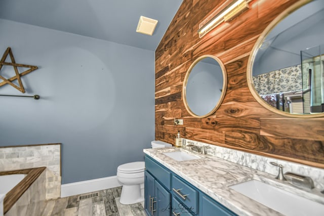 bathroom with wood walls, hardwood / wood-style floors, vanity, toilet, and vaulted ceiling