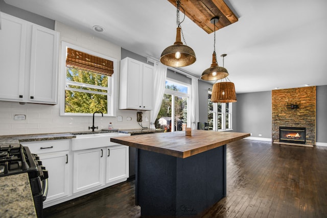 kitchen featuring dark wood-type flooring, white cabinets, hanging light fixtures, a kitchen island, and wood counters