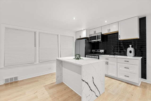 kitchen featuring white cabinets, a kitchen island, light stone countertops, and stainless steel appliances