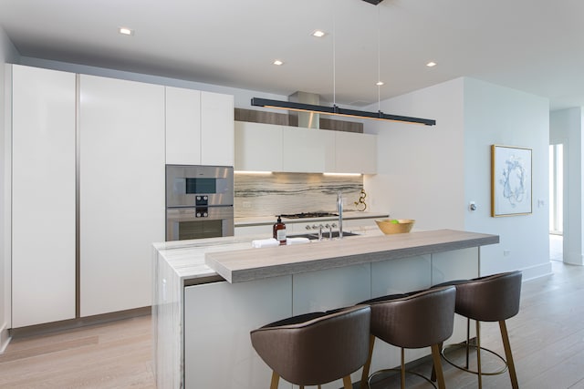 kitchen with white cabinetry, light wood-type flooring, a center island with sink, and decorative light fixtures