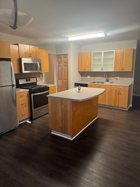 kitchen with stainless steel appliances, a center island, sink, dark hardwood / wood-style floors, and backsplash