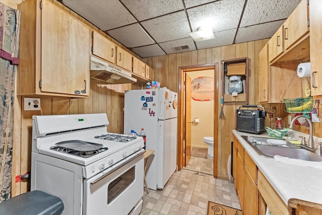 kitchen featuring a paneled ceiling, light brown cabinetry, wooden walls, sink, and white appliances