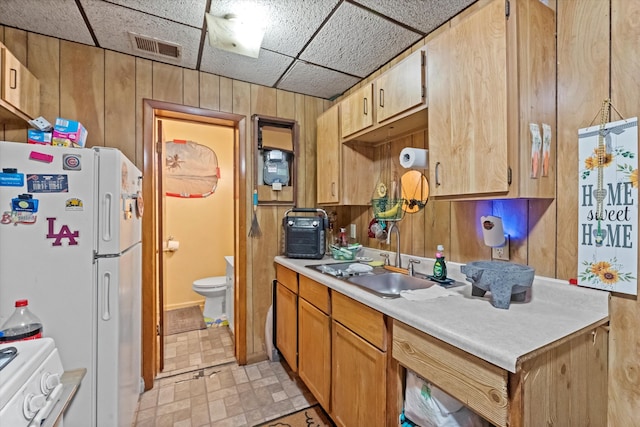 kitchen with a drop ceiling, wooden walls, sink, and white refrigerator