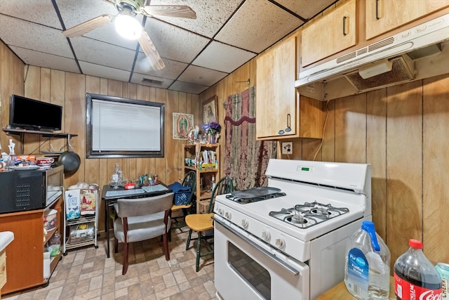 kitchen featuring white gas range, ceiling fan, a paneled ceiling, and wooden walls