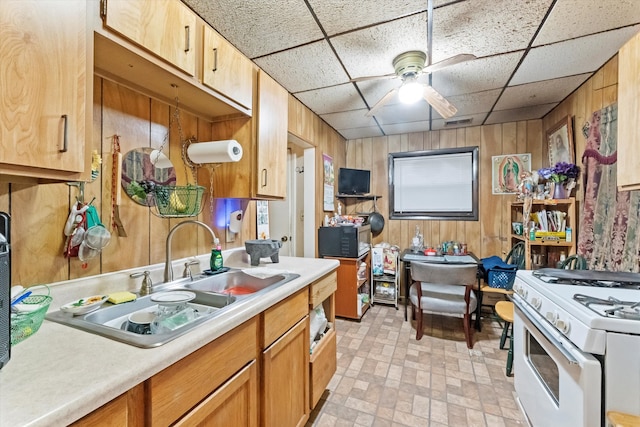 kitchen with wood walls, sink, white range with gas cooktop, and a drop ceiling