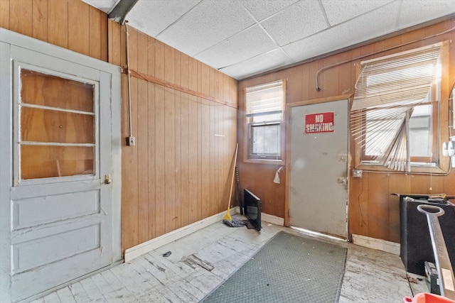 doorway to outside featuring wooden walls and a drop ceiling