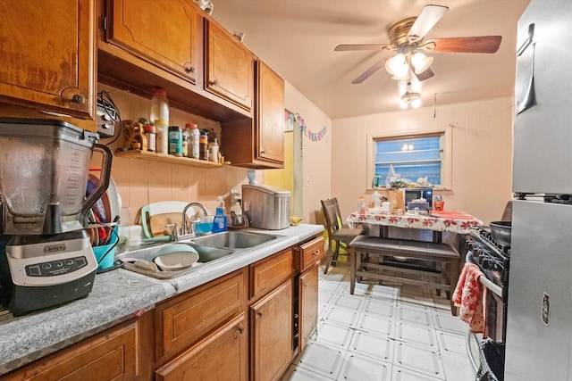 kitchen featuring black range with gas stovetop, sink, ceiling fan, and stainless steel refrigerator