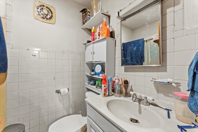 bathroom featuring a shower with shower door, vanity, toilet, and tile walls