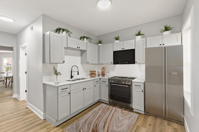 kitchen with stainless steel gas range oven, sink, light hardwood / wood-style flooring, backsplash, and refrigerator with ice dispenser