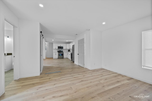 unfurnished living room featuring a barn door and light wood-type flooring