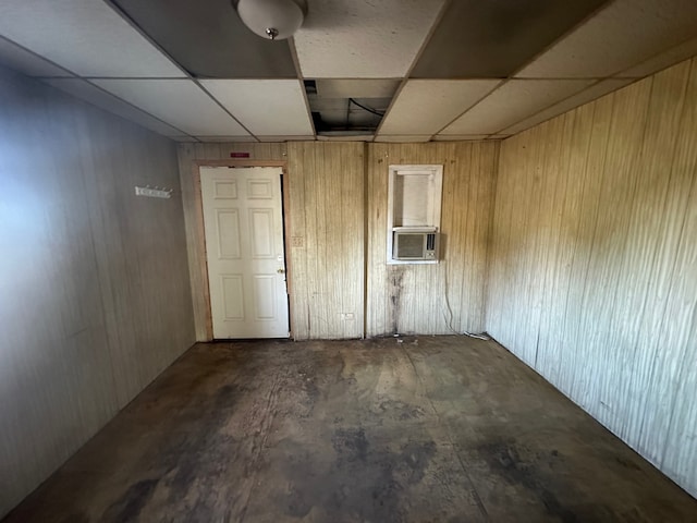 basement featuring a drop ceiling, cooling unit, and wooden walls