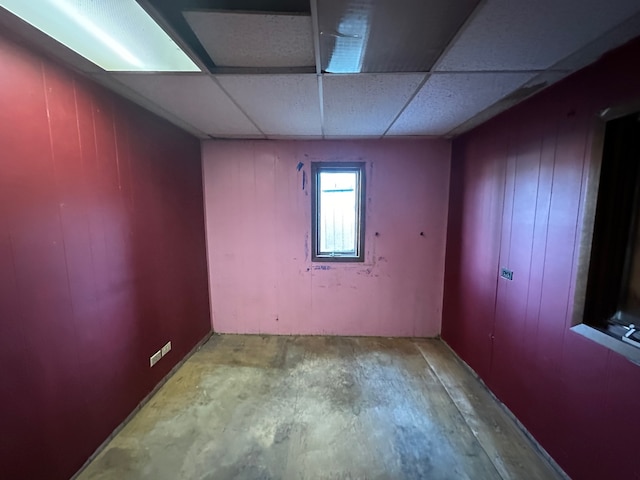 empty room featuring concrete flooring, a paneled ceiling, and wooden walls