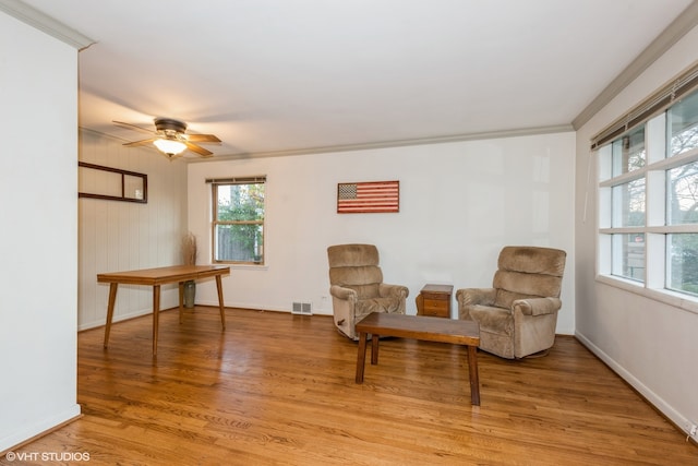 living area featuring hardwood / wood-style floors, ceiling fan, and crown molding