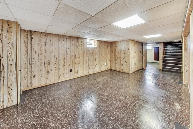 basement with a drop ceiling and wood walls