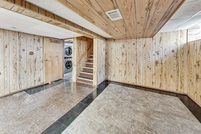 basement featuring wooden walls, stacked washer and dryer, and wood ceiling