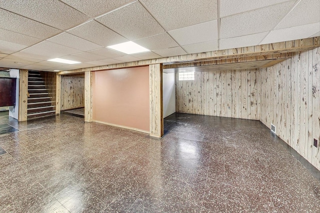 basement featuring a drop ceiling and wood walls