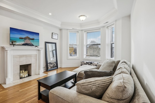 living room featuring a tiled fireplace, crown molding, a tray ceiling, and light hardwood / wood-style flooring