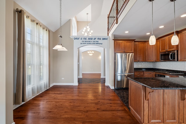 kitchen with appliances with stainless steel finishes, dark hardwood / wood-style flooring, tasteful backsplash, hanging light fixtures, and a breakfast bar area