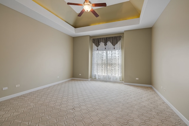 carpeted spare room with a tray ceiling and ceiling fan