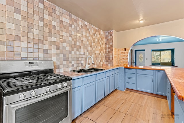 kitchen with wooden counters, backsplash, gas stove, sink, and blue cabinetry