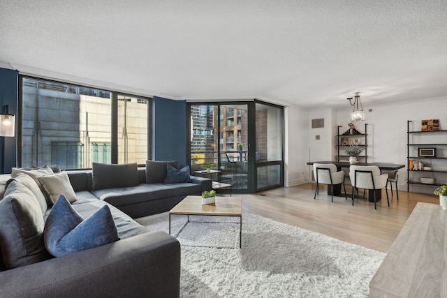 living room with a healthy amount of sunlight, a wall of windows, a textured ceiling, and light hardwood / wood-style flooring