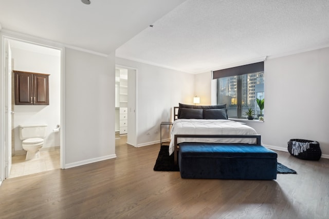 bedroom with a textured ceiling, ornamental molding, dark wood-type flooring, and ensuite bath