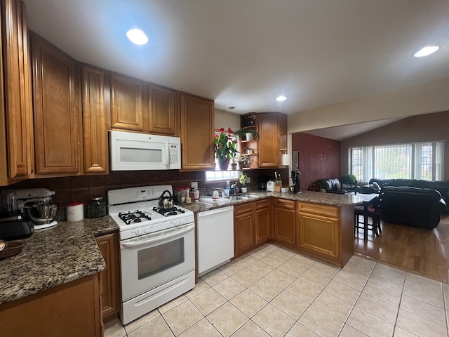 kitchen featuring white appliances, dark stone counters, sink, decorative backsplash, and kitchen peninsula