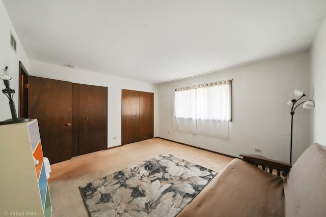 bedroom featuring light colored carpet and multiple closets