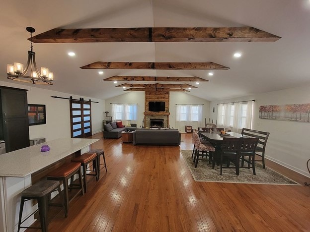 dining room featuring a fireplace, wood-type flooring, a barn door, and lofted ceiling with beams