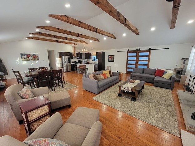 living room featuring a barn door, light hardwood / wood-style flooring, and lofted ceiling with beams