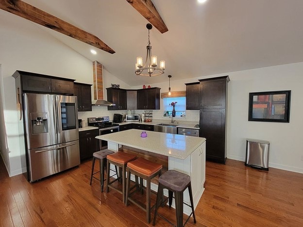 kitchen with a kitchen bar, stainless steel appliances, beam ceiling, hardwood / wood-style floors, and a kitchen island