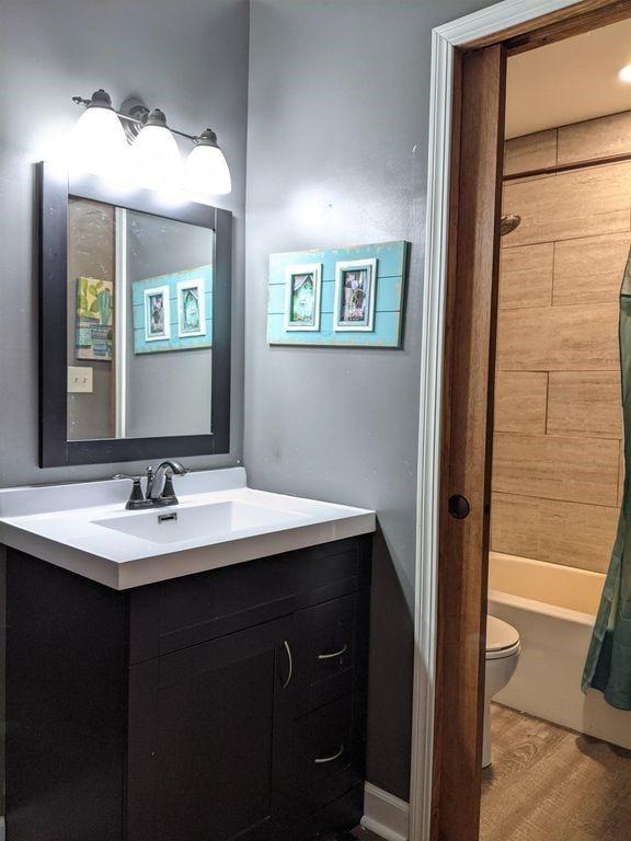 full bathroom featuring hardwood / wood-style flooring, shower / bath combo with shower curtain, vanity, and toilet