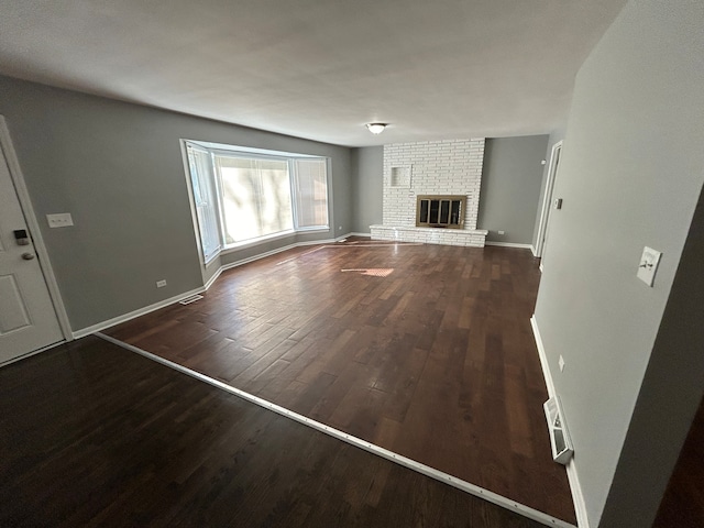 unfurnished living room with a brick fireplace and dark hardwood / wood-style flooring