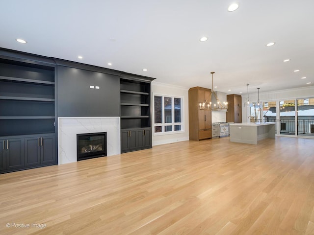 unfurnished living room with ornamental molding, a fireplace, light wood-style flooring, and an inviting chandelier