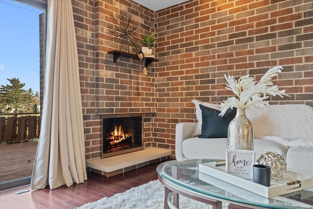 sitting room with hardwood / wood-style flooring, brick wall, and a brick fireplace