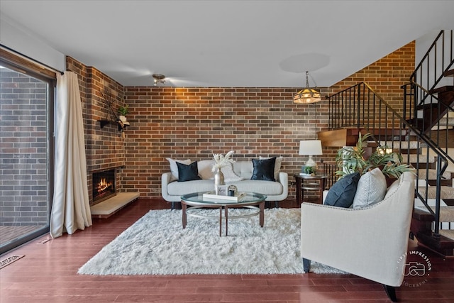 living room featuring a brick fireplace, dark wood-type flooring, and brick wall