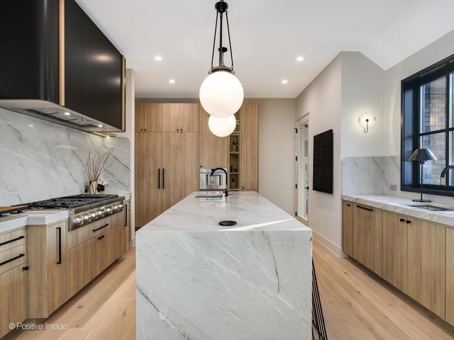 kitchen with wall chimney range hood, a large island, light hardwood / wood-style floors, light stone counters, and stainless steel gas cooktop