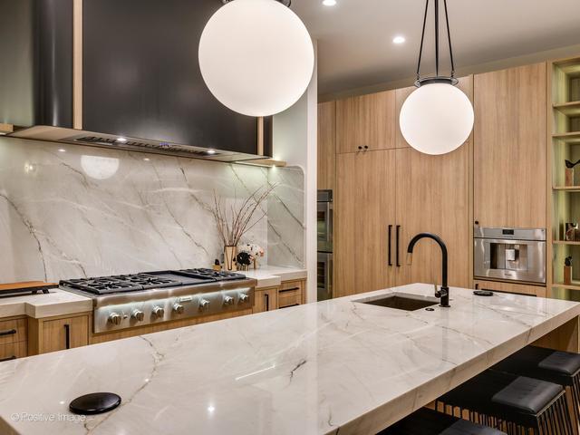 kitchen with light stone countertops, backsplash, sink, wall chimney range hood, and pendant lighting