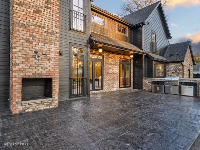 patio terrace at dusk featuring a fireplace, an outdoor kitchen, and area for grilling