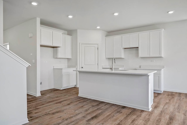 kitchen with white cabinets, a center island with sink, sink, and light wood-type flooring