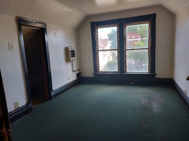 additional living space featuring dark carpet, heating unit, and vaulted ceiling