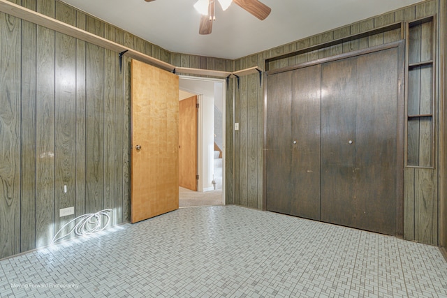 unfurnished bedroom featuring ceiling fan, wood walls, and a closet