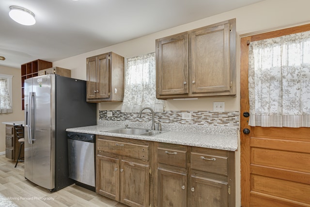 kitchen with backsplash, sink, appliances with stainless steel finishes, and light wood-type flooring